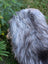 A fluffy dog with silver and dark gray fur lying on a fall massive icelandic natural grey sheepskin wool icelandic rug