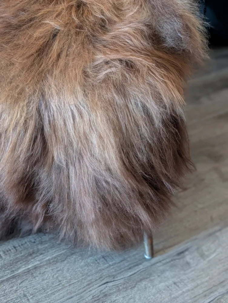 A plush icelandic sheepskin ottoman with long brown and gray wool icelandic fur and sleek metal leg