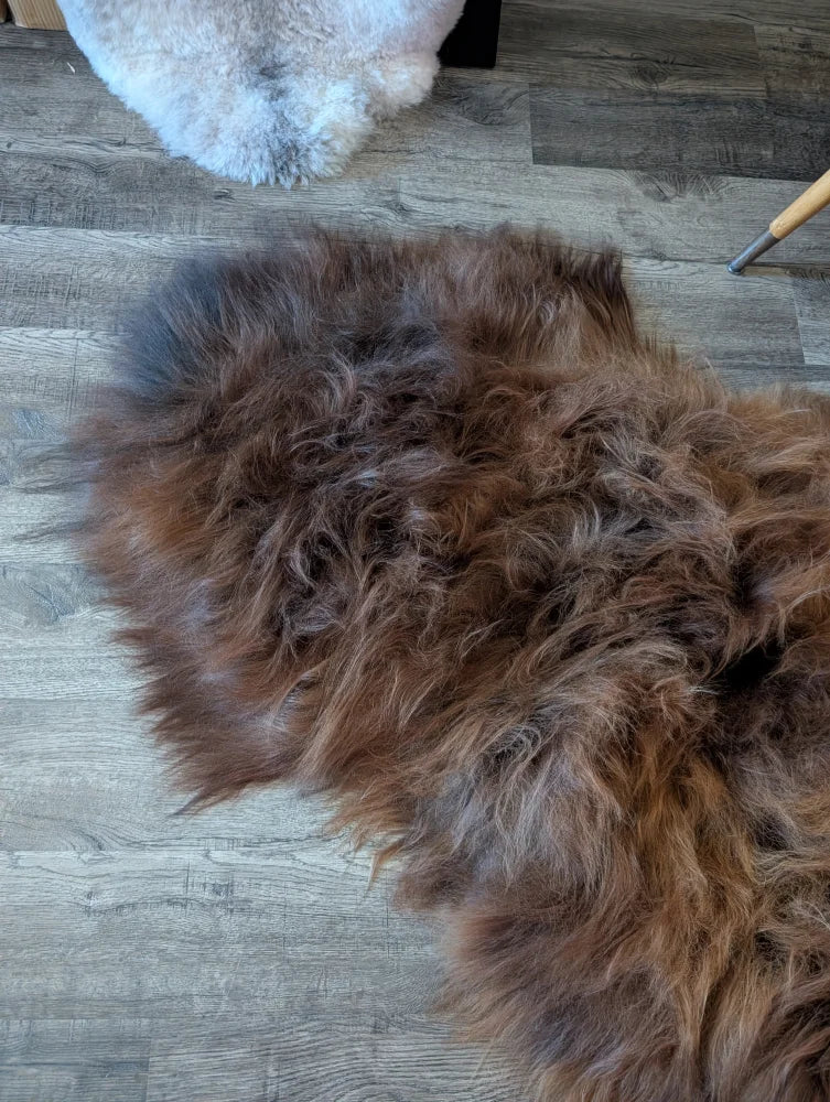 A plush irregular dark rusty icelandic sheepskin rug with thick shaggy wool on a wooden floor for cozy decor