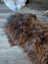 A plush irregular dark rusty icelandic sheepskin rug with thick shaggy wool on a wooden floor for cozy decor
