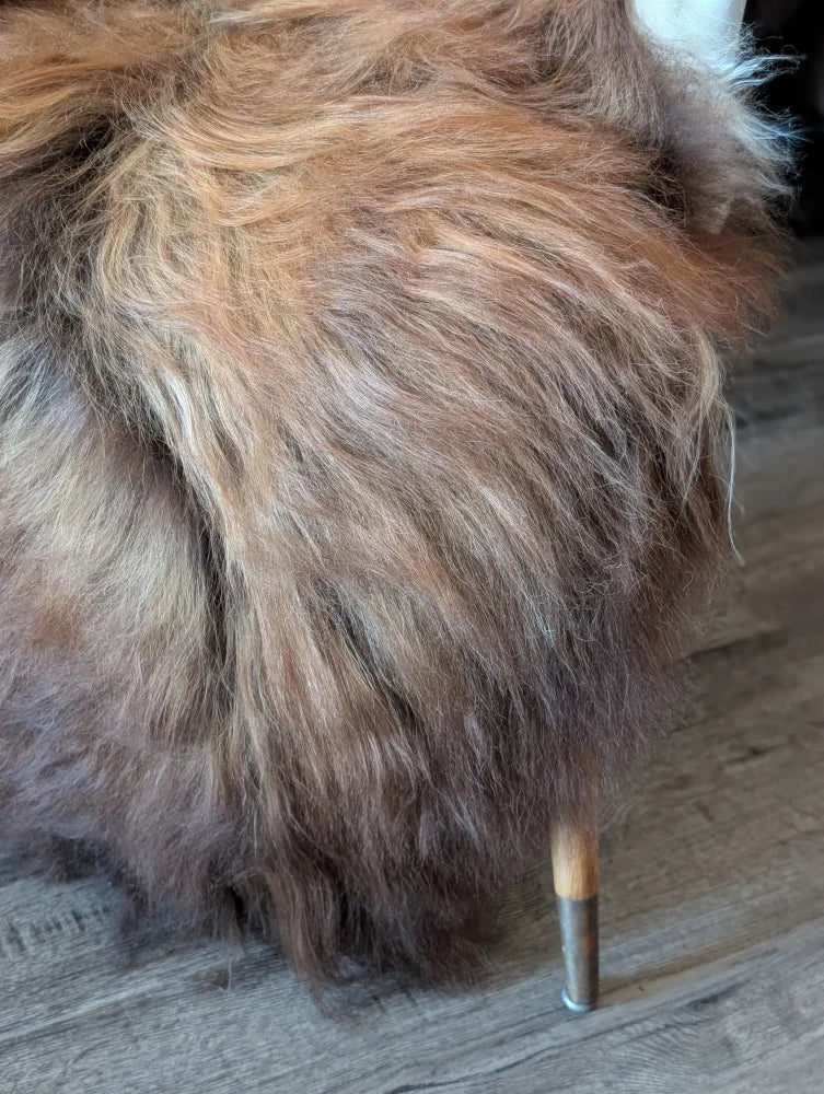 A plush shaggy brown and tan icelandic sheepskin ottoman with wooden legs in natural dark rusty colors