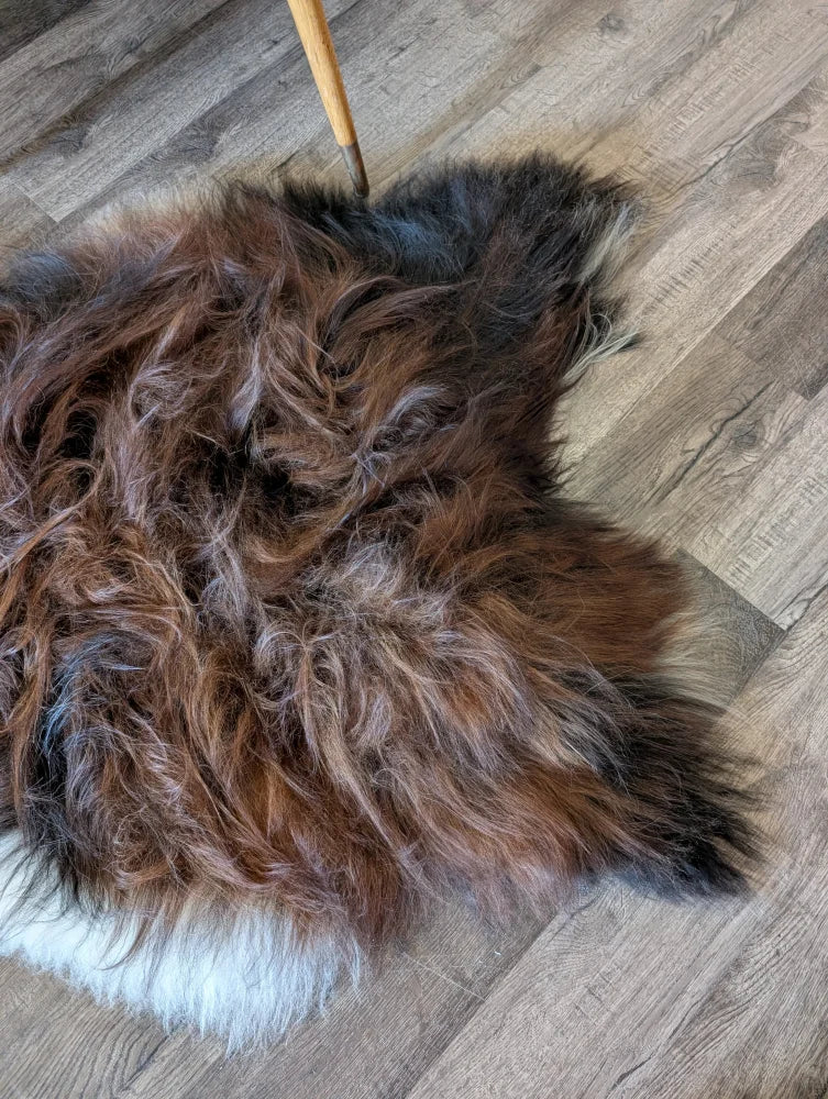 A plush irregular brown and black icelandic sheepskin rug with white border on wooden floor perfect for cozy decor