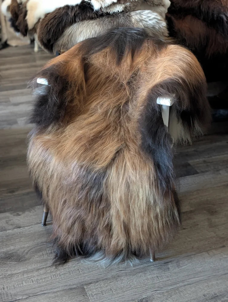 A plush stool covered in multi toned brown and black icelandic sheepskin with a sleek metal frame