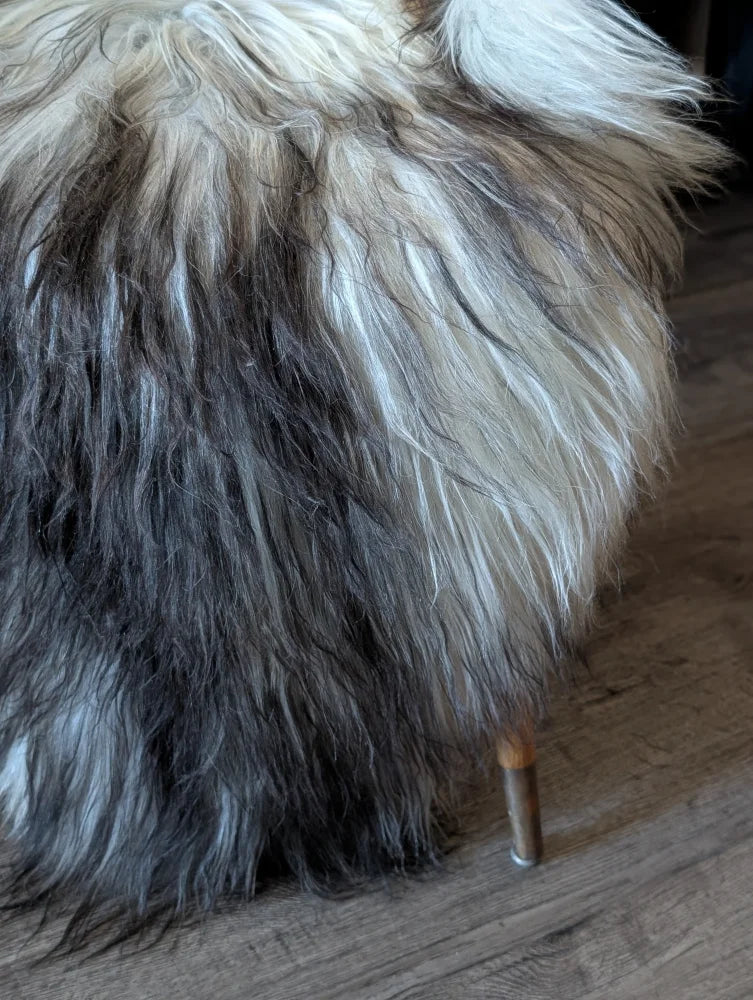 A plush shaggy wool icelandic ottoman with gradient white to dark gray strands and wooden legs for cozy seating