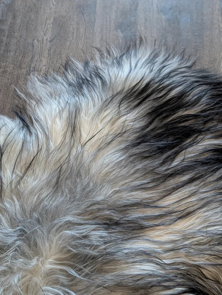 A plush multicolored faux fur rug with long wool icelandic texture in natural grey black and cream tones