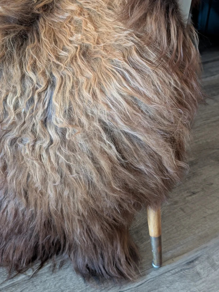 A plush curly brown and beige wool icelandic sheepskin-covered stool with wooden legs from fall6 collection