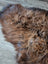 A massive natural dark rusty icelandic sheepskin rug with thick curly wool icelandic texture and irregular shape