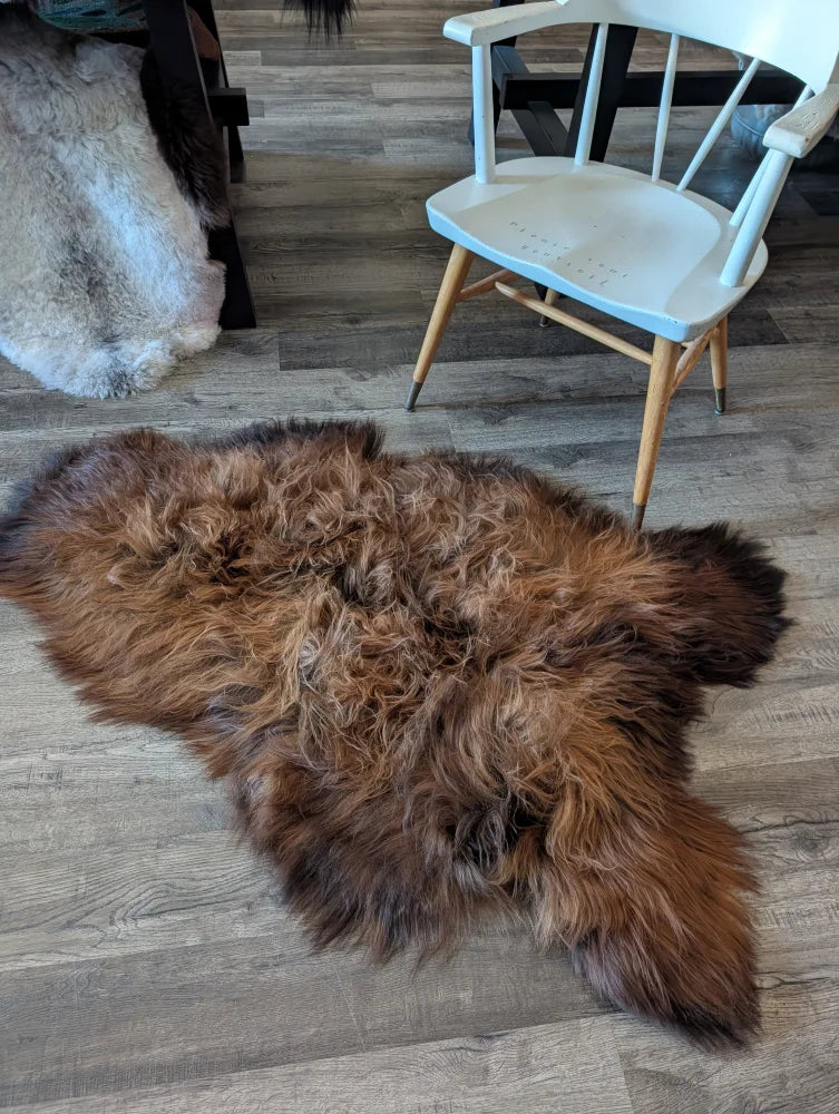 A plush irregular brown wool icelandic sheepskin rug with thick natural fur texture on a wooden floor