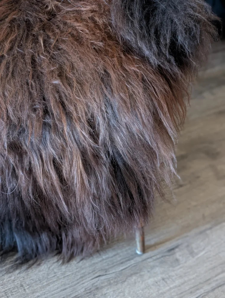 A plush shaggy brown and black wool icelandic faux fur ottoman with a single metallic leg perfect for cozy spaces