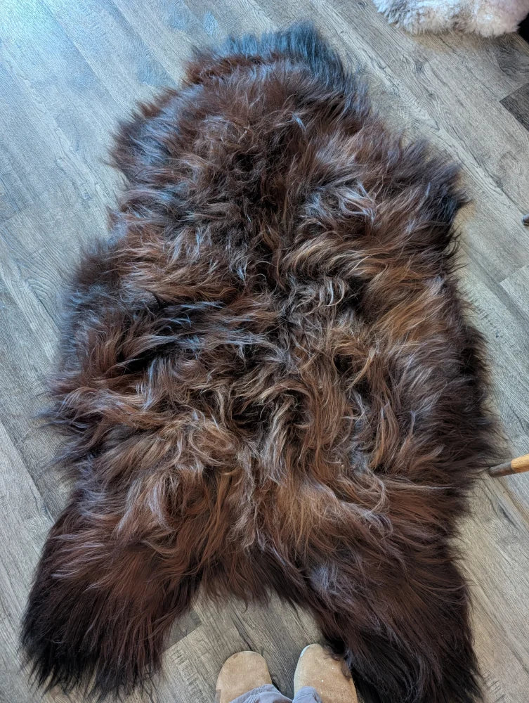 A thick shaggy brown and black wool icelandic sheepskin rug with natural untamed texture on wooden floor