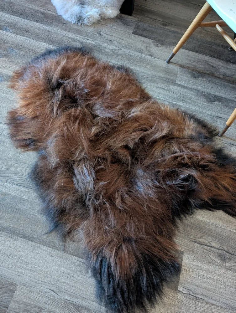 A plush irregular icelandic sheepskin rug in natural dark rusty shades with thick wool icelandic fur on wooden floor