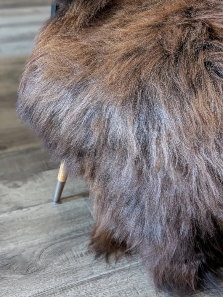 A plush thick brown and gray wool icelandic sheepskin throw draped over a modern chair leg for cozy décor