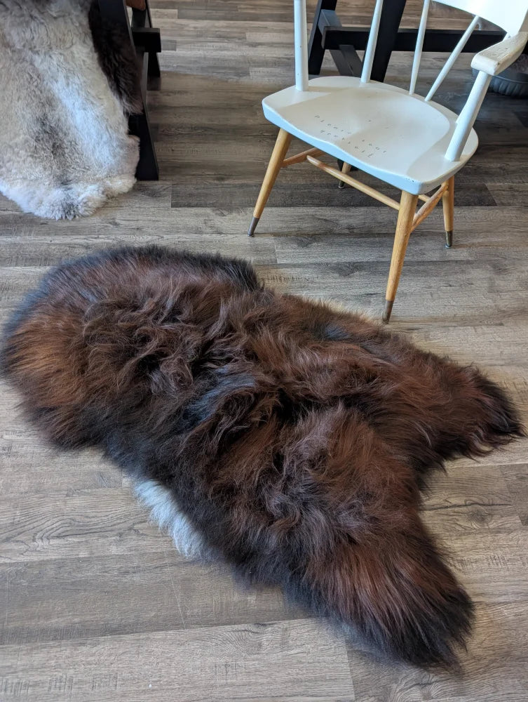 A plush irregularly shaped dark rusty brown and black icelandic sheepskin rug with soft wool texture on wooden floor