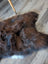A plush irregular dark rusty icelandic sheepskin rug with soft shaggy wool icelandic fur on wooden floor