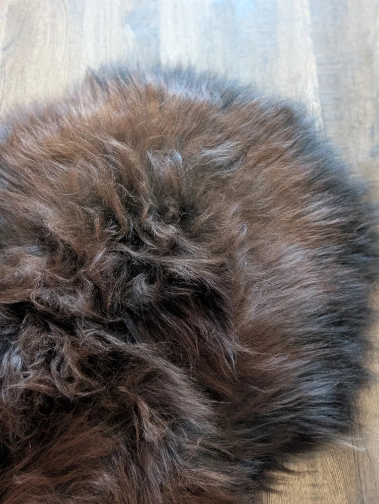 A plush circular icelandic sheepskin rug in dark rusty brown and black with soft wool icelandic fibers