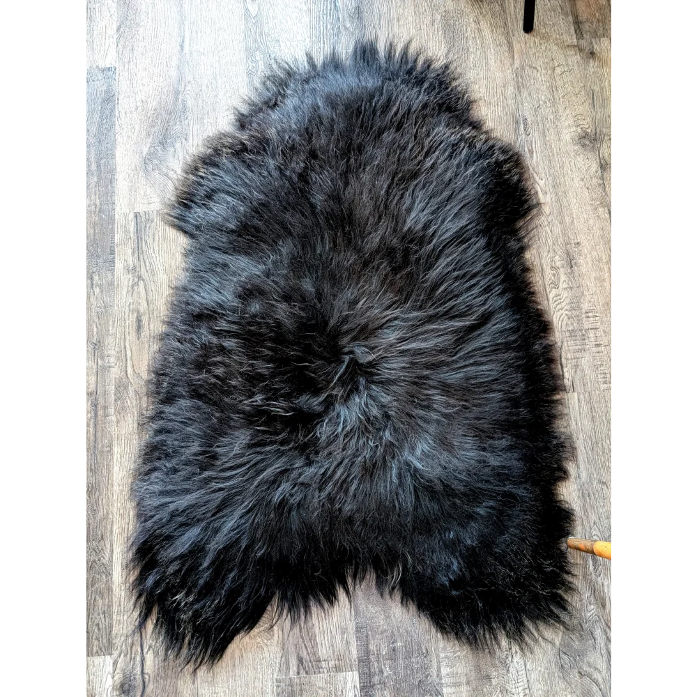 A plush dark gray black icelandic sheepskin rug with thick fluffy texture and natural irregular edges