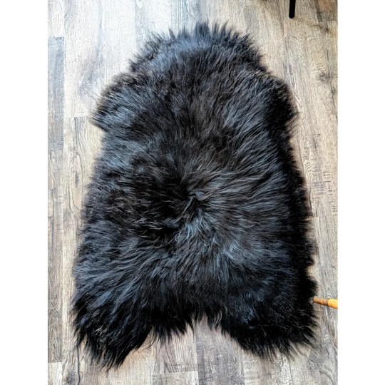 A plush dark gray black icelandic sheepskin rug with thick fluffy texture and natural irregular edges