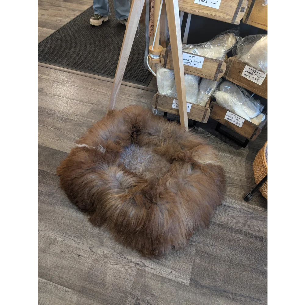 Cozy highland sheepskin pet bed with brown wool rug, wood legs, metal base