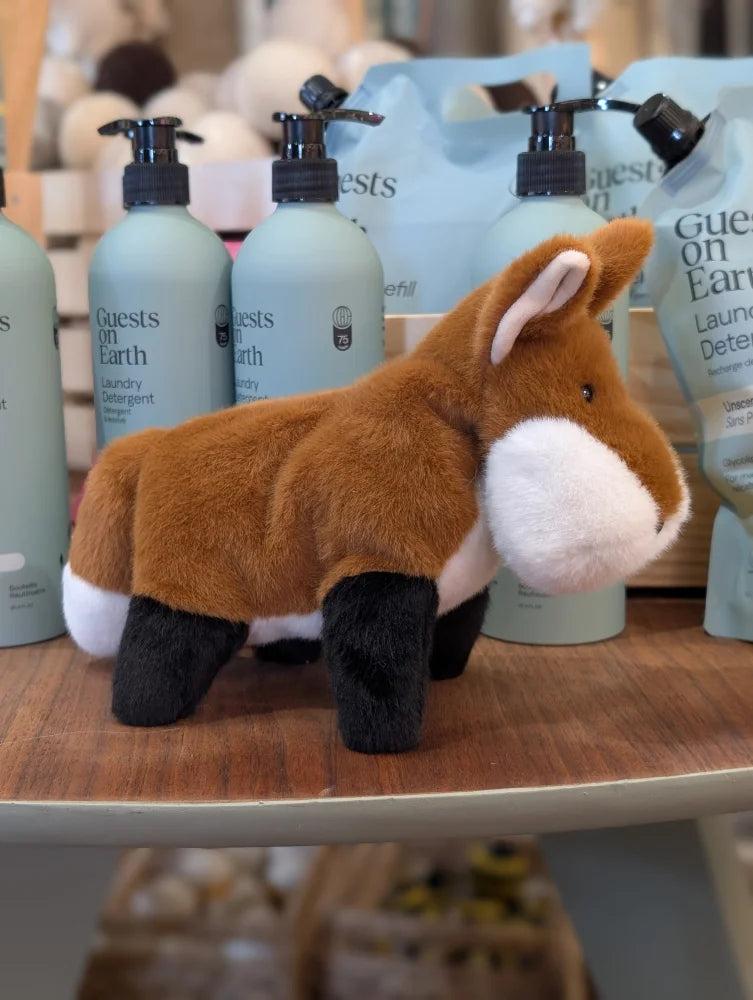 A plush frank the fox stuffed animal with brown white and black fur standing on a wooden shelf