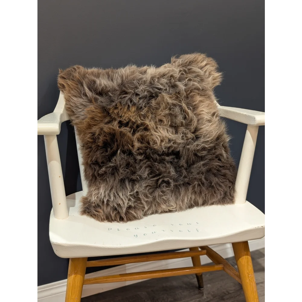 A gorgeous british sheepskin cushion with plush shaggy brown fur on unbleached cotton canvas resting on white chair