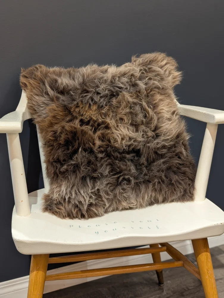 A gorgeous british sheepskin cushion with plush shaggy brown fur on unbleached cotton canvas resting on white chair