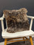 A gorgeous british sheepskin cushion with plush shaggy brown fur on unbleached cotton canvas resting on white chair