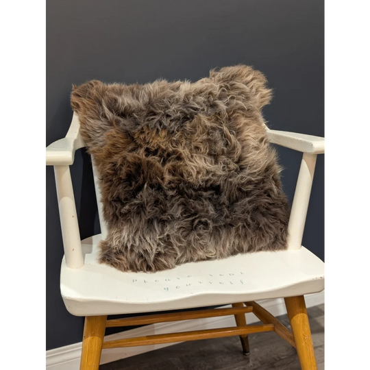 A gorgeous british sheepskin cushion with plush shaggy brown fur on unbleached cotton canvas resting on white chair