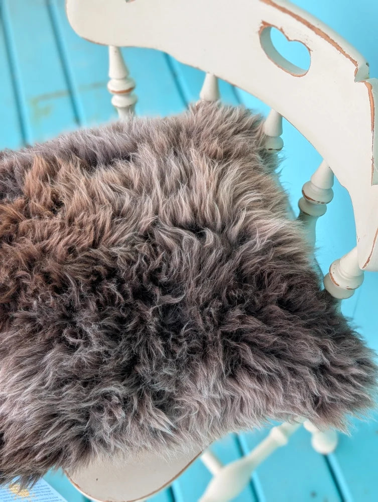 A plush shaggy gray british sheepskin cushion with soft curly texture on white chair by angus oliver on unbleached cotton canvas