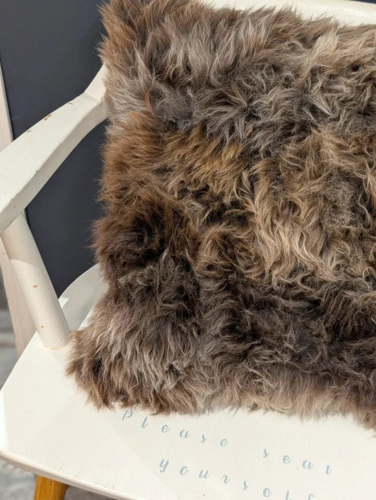 A gorgeous british sheepskin cushion with plush brown and gray faux fur on unbleached cotton canvas white chair