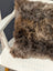 A gorgeous british sheepskin cushion with plush brown and gray faux fur on unbleached cotton canvas white chair