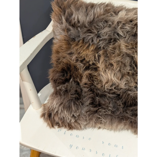 A gorgeous british sheepskin cushion with plush brown and gray faux fur on unbleached cotton canvas white chair