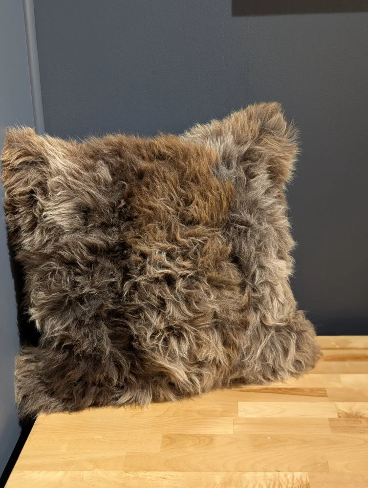 Gorgeous british sheepskin cushion with plush shaggy brown and gray curly texture on unbleached cotton canvas