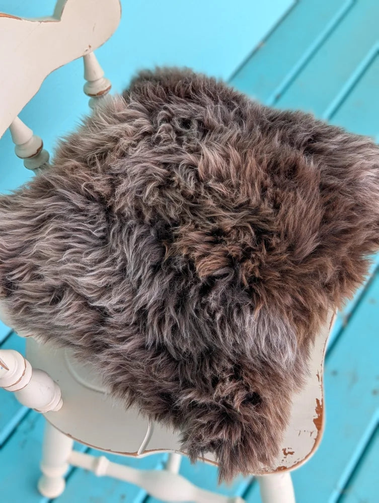 A plush gray british sheepskin cushion with soft curly texture on a white chair by angus oliver unbleached cotton canvas