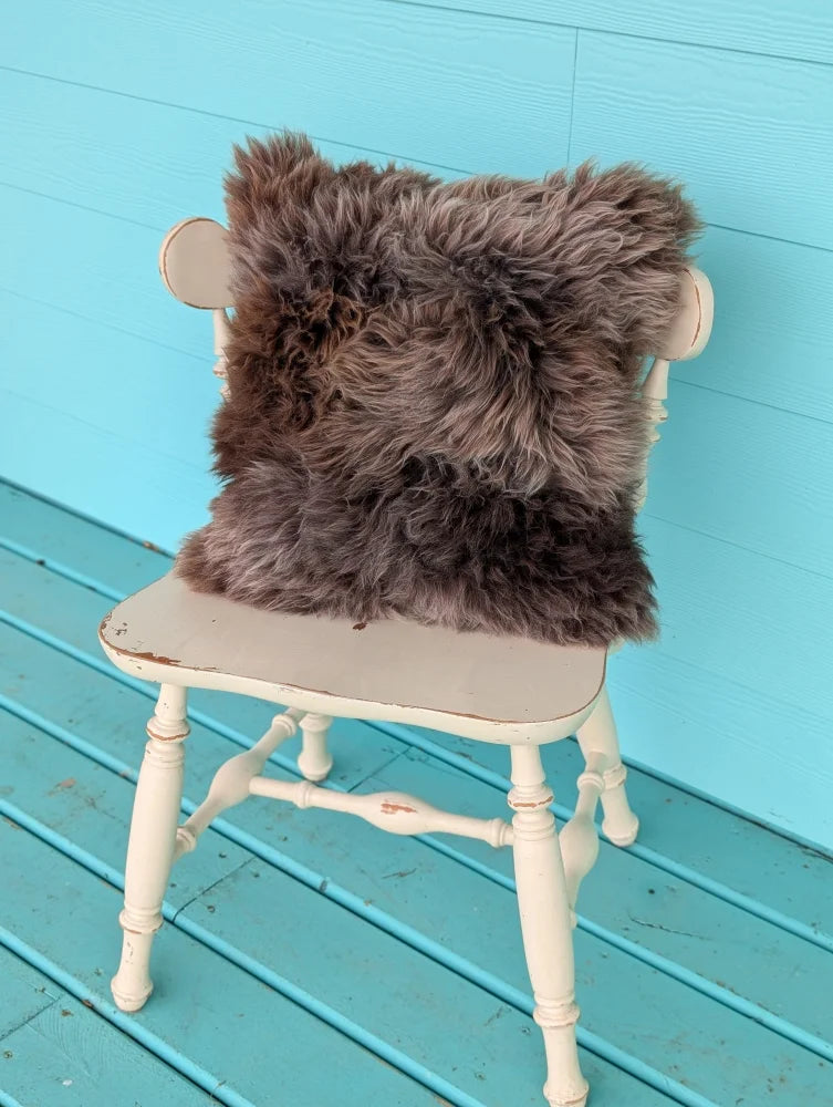 A dark gray british sheepskin cushion with soft shaggy texture on an antique white chair by angus oliver