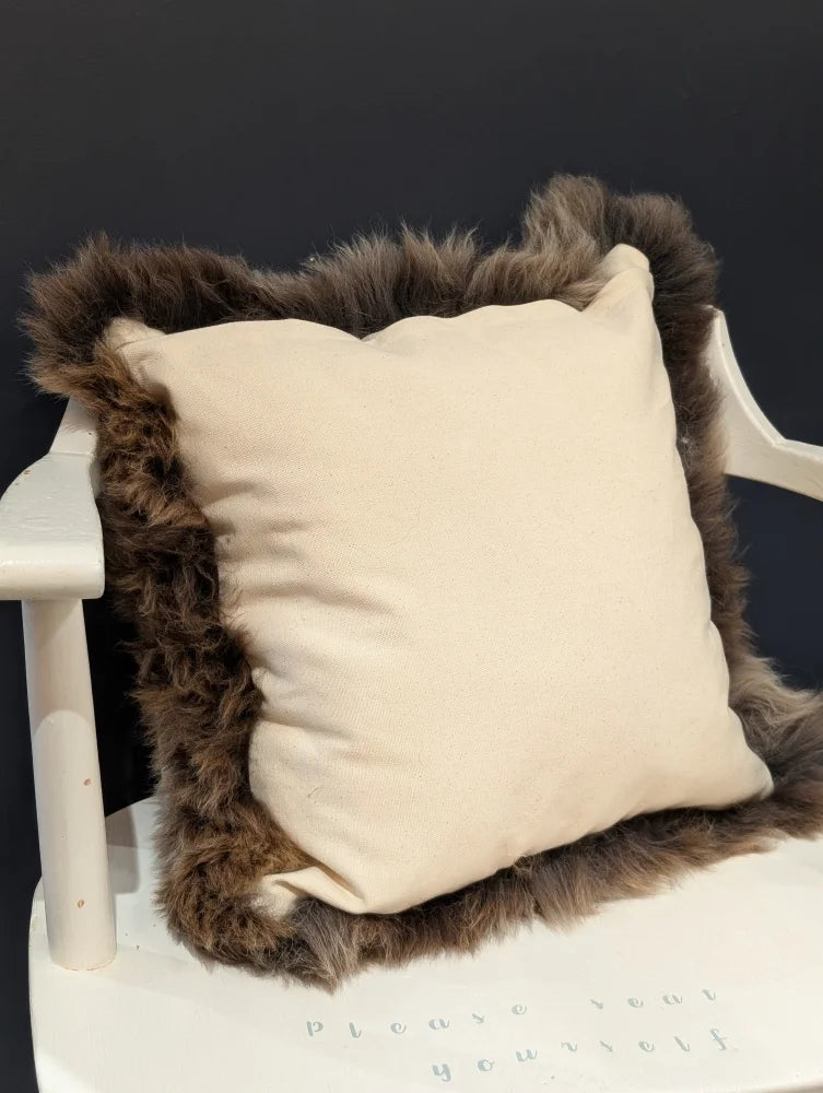 Cream-colored british sheepskin cushion with plush dark brown fur trim on unbleached cotton canvas fabric