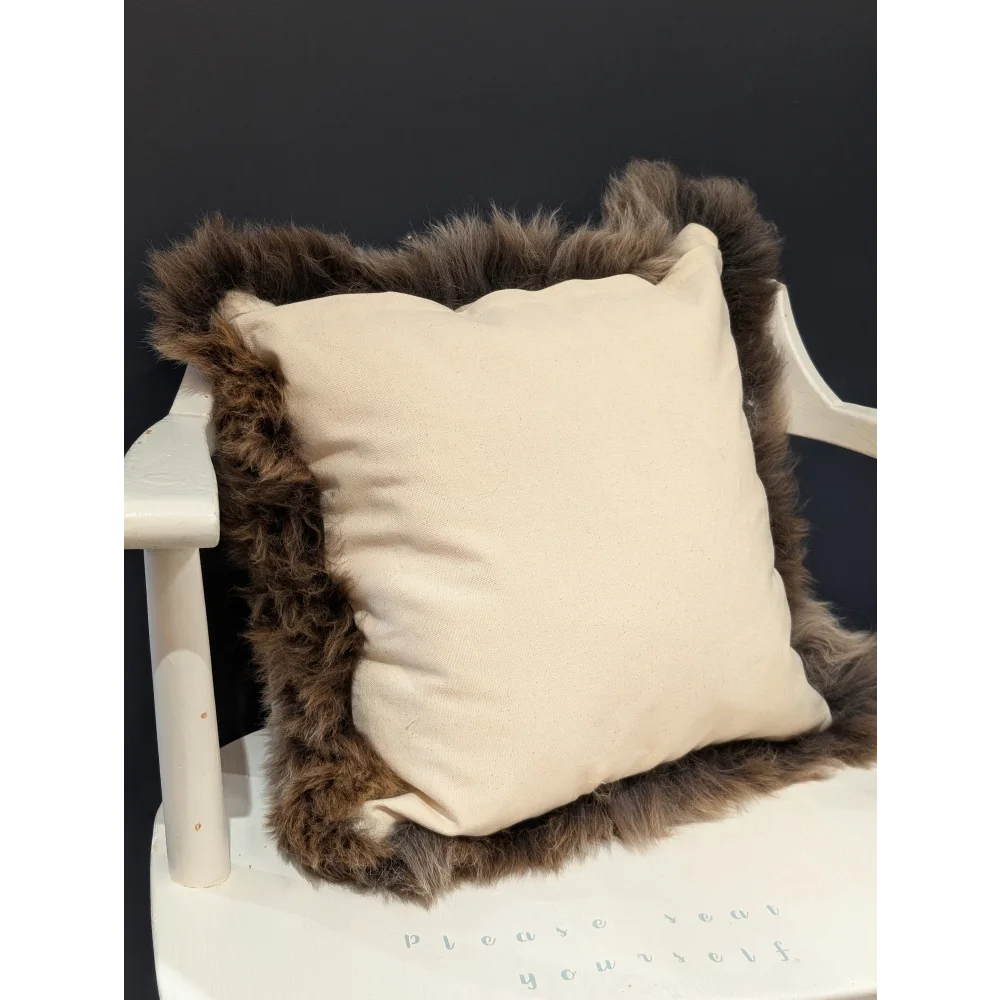Cream-colored british sheepskin cushion with plush dark brown fur trim on unbleached cotton canvas fabric