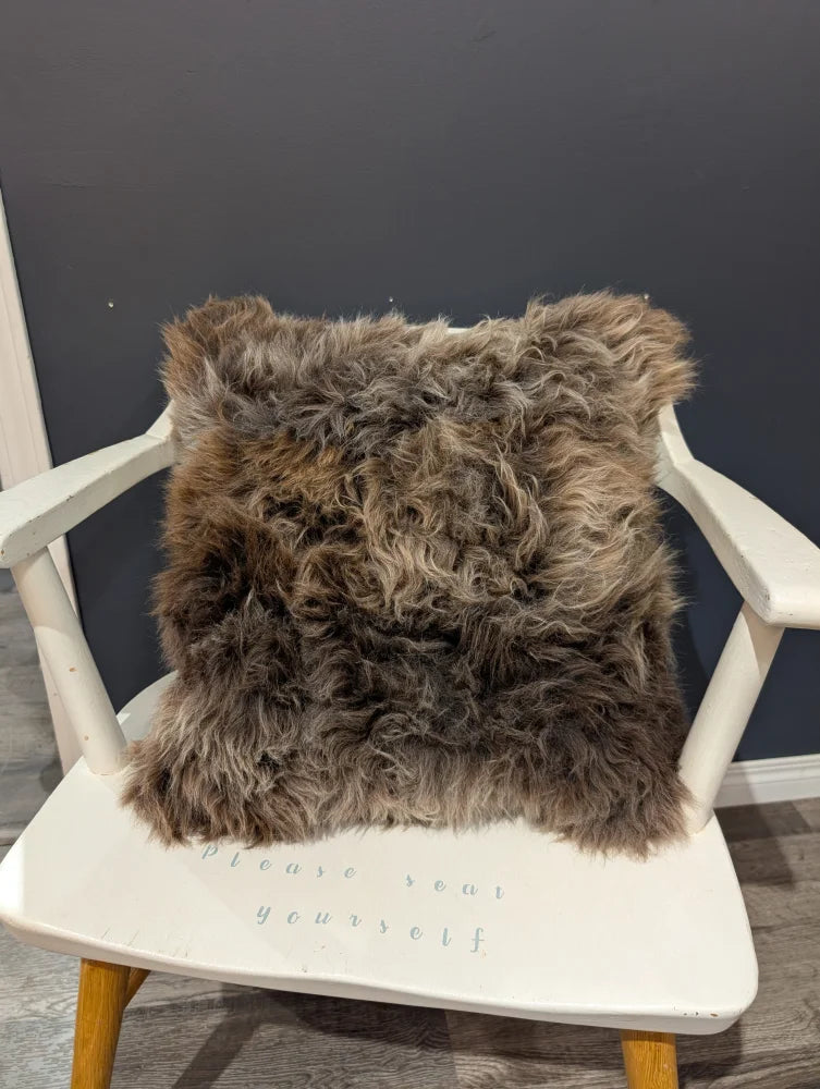Gorgeous british sheepskin cushion with plush shaggy brown texture on a white chair made with unbleached cotton canvas