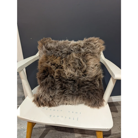 Gorgeous british sheepskin cushion with plush shaggy brown texture on a white chair made with unbleached cotton canvas