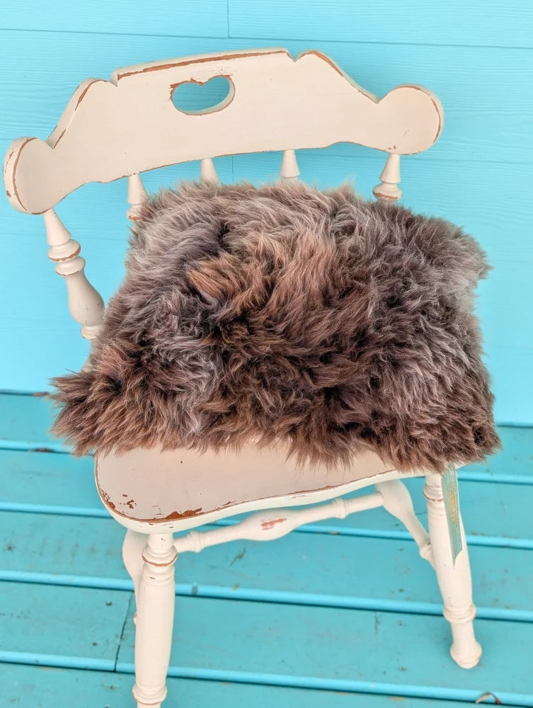 A gorgeous british sheepskin cushion in shaggy brown on a distressed white chair made with unbleached cotton canvas by angus oliver