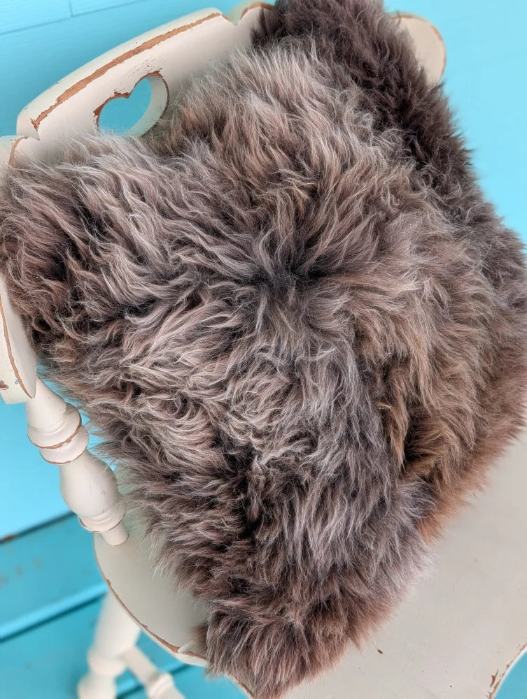 A plush gray british sheepskin cushion made with unbleached cotton canvas draped over a white wooden chair by angus oliver