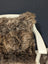 A plush curly brown british sheepskin cushion draped over a white wooden chair arm on unbleached cotton canvas