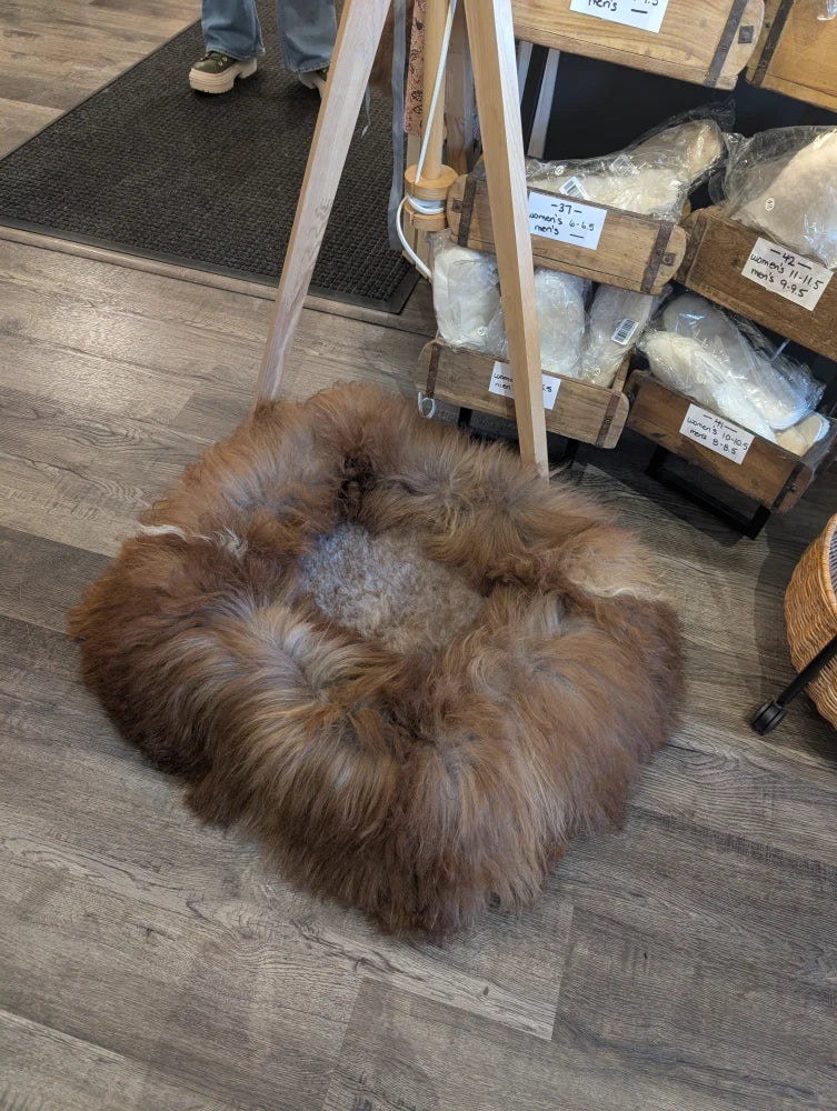 Cozy highland sheepskin pet bed with brown wool rug, wood legs, metal base