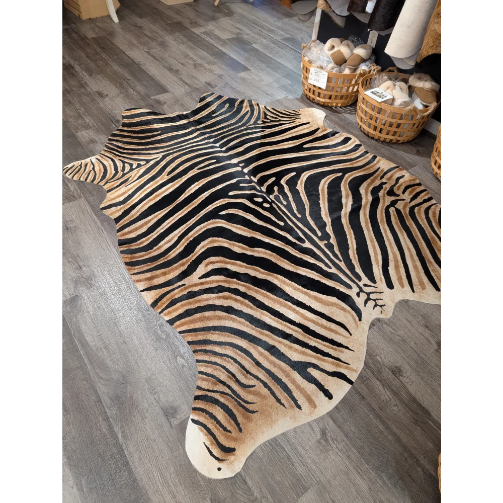 A gorgeous zebra printed large cowhide rug by angus oliver with bold black and tan stripes and unique characteristics on gray wood floor