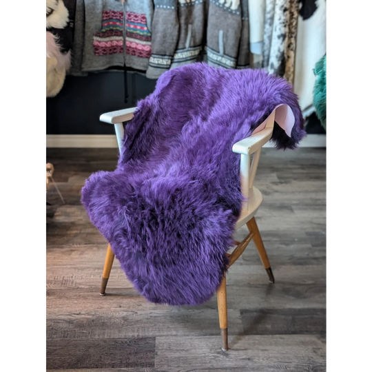 Gorgeous grape purple merino sheepskin throw on wooden arms with brass legs