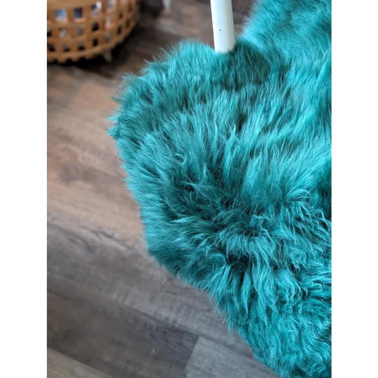 Teal fluffy duster with white handle on gorgeous merino sheepskin