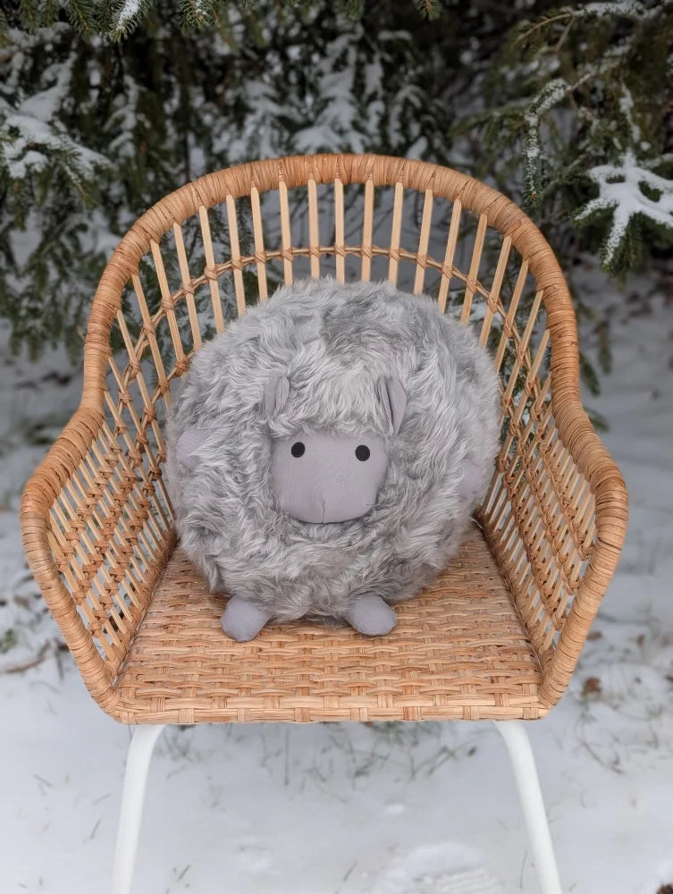 A soft fluffy grey rotund sheep cushion made of merino sheepskin sits on a wicker chair by angus oliver clearance