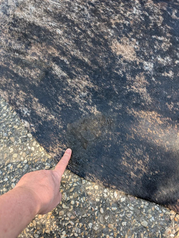 A hand points to a large cowhide rug with unique black and brown patches showing rustic charm