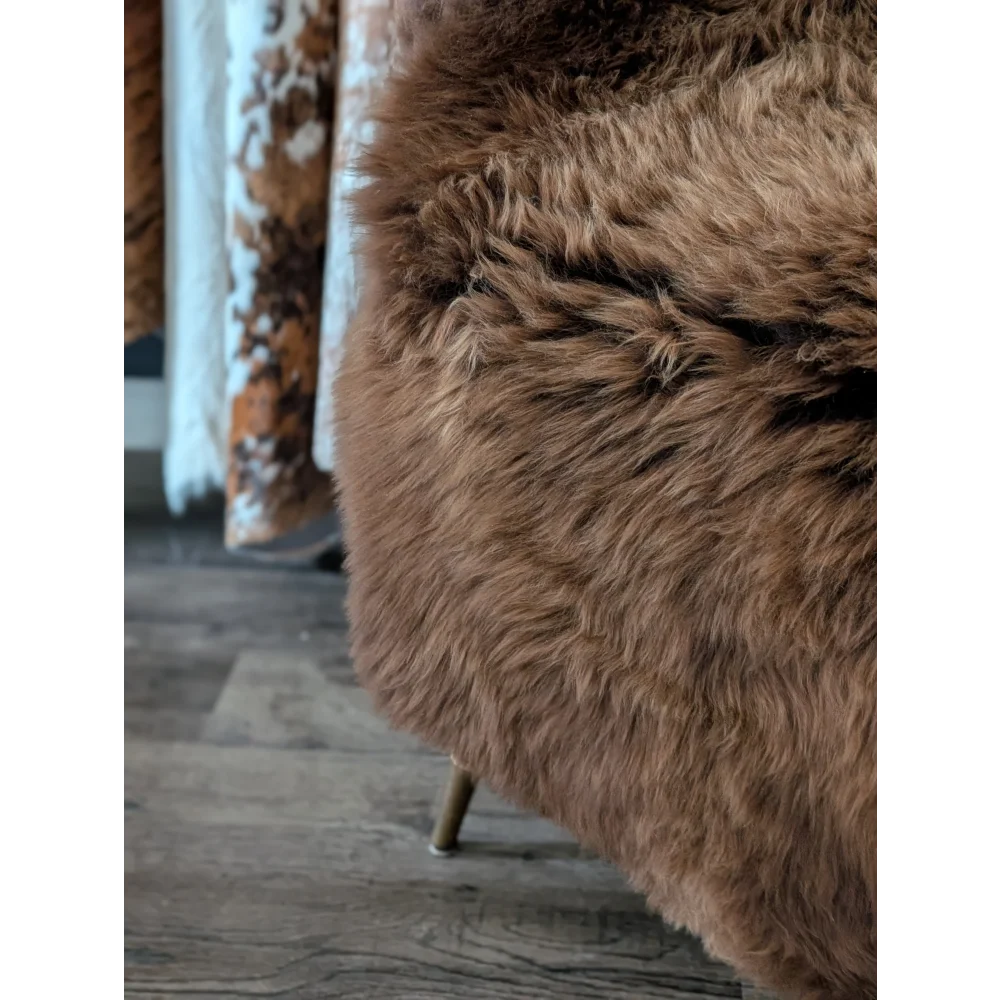 A large british plush brown sheepskin throw draped over a modern chair with slender metal legs