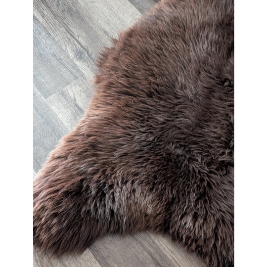 A plush dark brown angus oliver sheepskin rug with soft dense texture on gray wood floor perfect for cozy spaces
