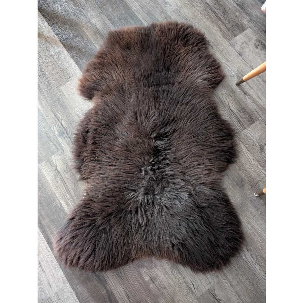 A plush extra large british sheepskin rug in dark brown with natural fluffy texture and irregular edges
